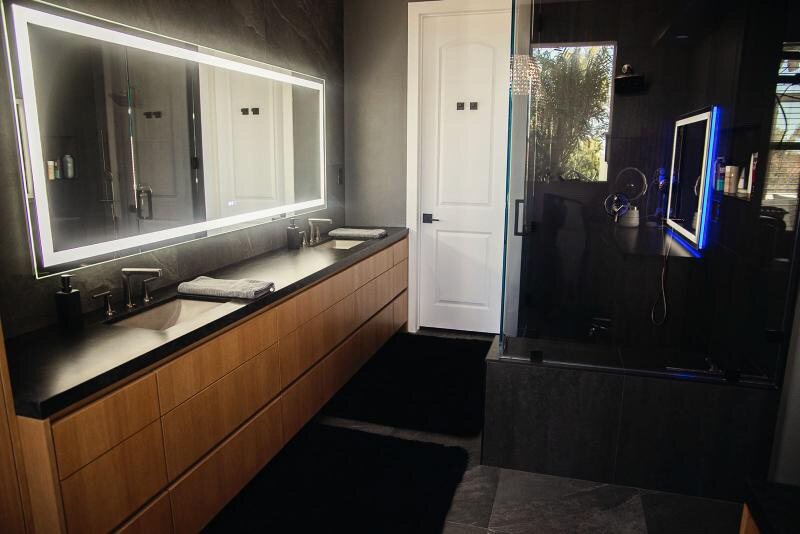 Finished black-and-walnut master bathroom remodel in Encinitas with a glass walk-in shower and backlit LED mirror