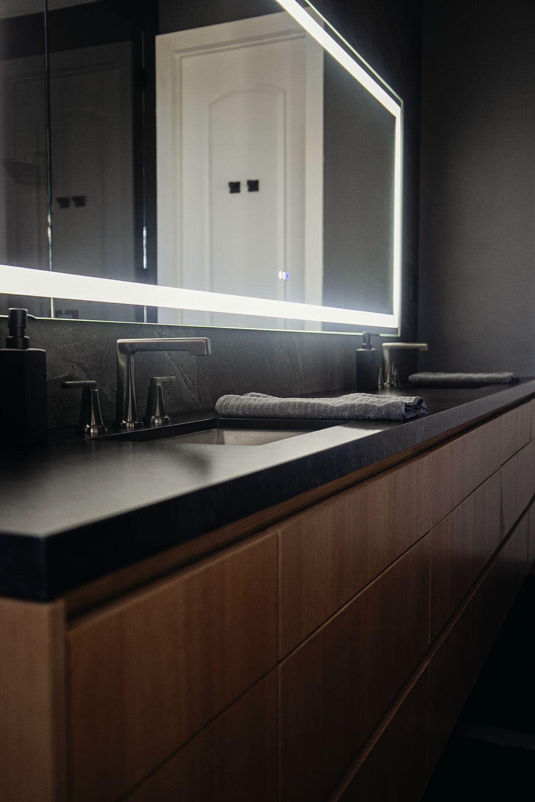 Finished walnut floating vanity with a honed black slate counter and backlit LED mirror