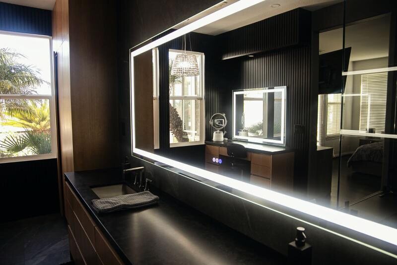 Dual vanity and makeup station with backlit LED mirrors in a dark master bath