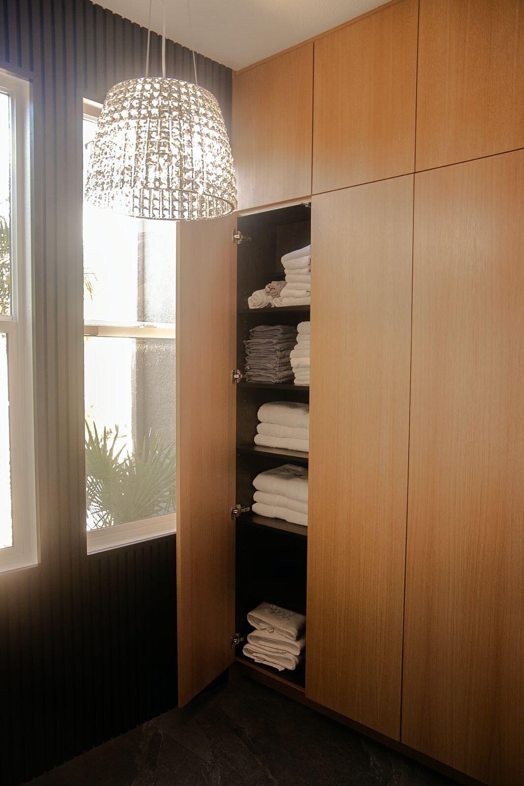 Custom built-in walnut linen cabinet with a crystal pendant light