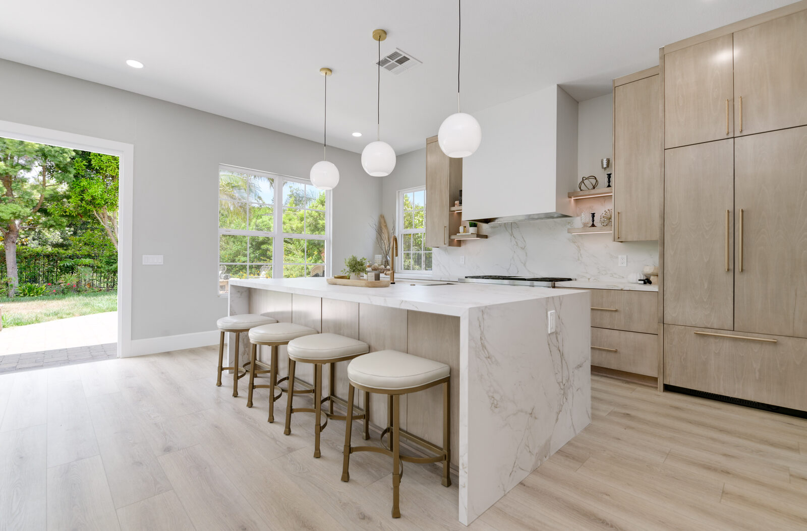 Open white-oak kitchen with a quartz island, bar seating and large garden windows