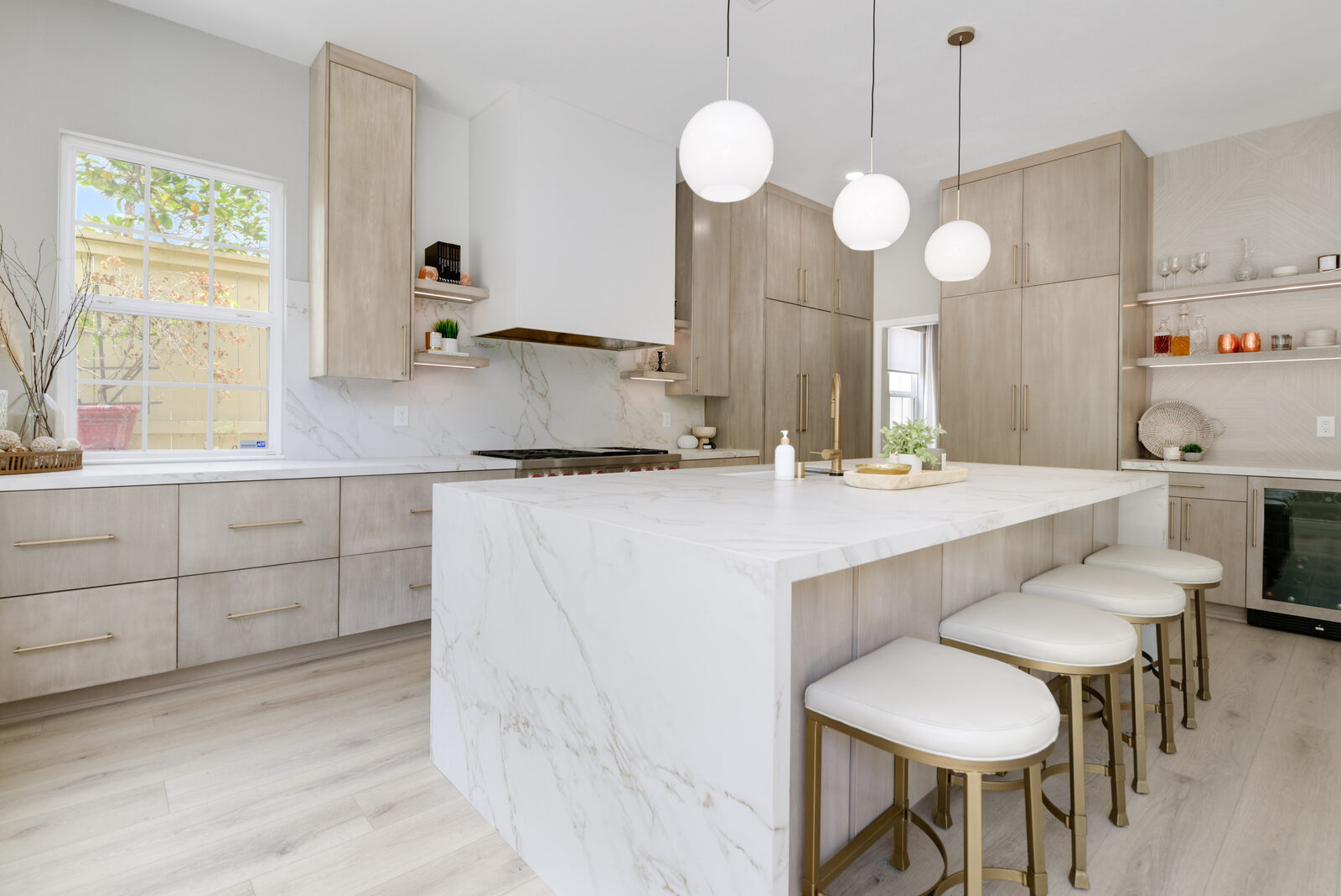 Waterfall quartz island with upholstered bar stools and a built-in beverage nook